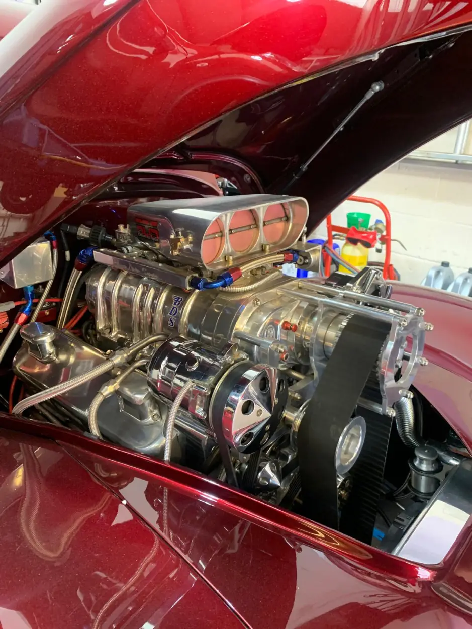Close-up of chrome supercharger setup and detailed engine components inside a burgundy Willys Coupe